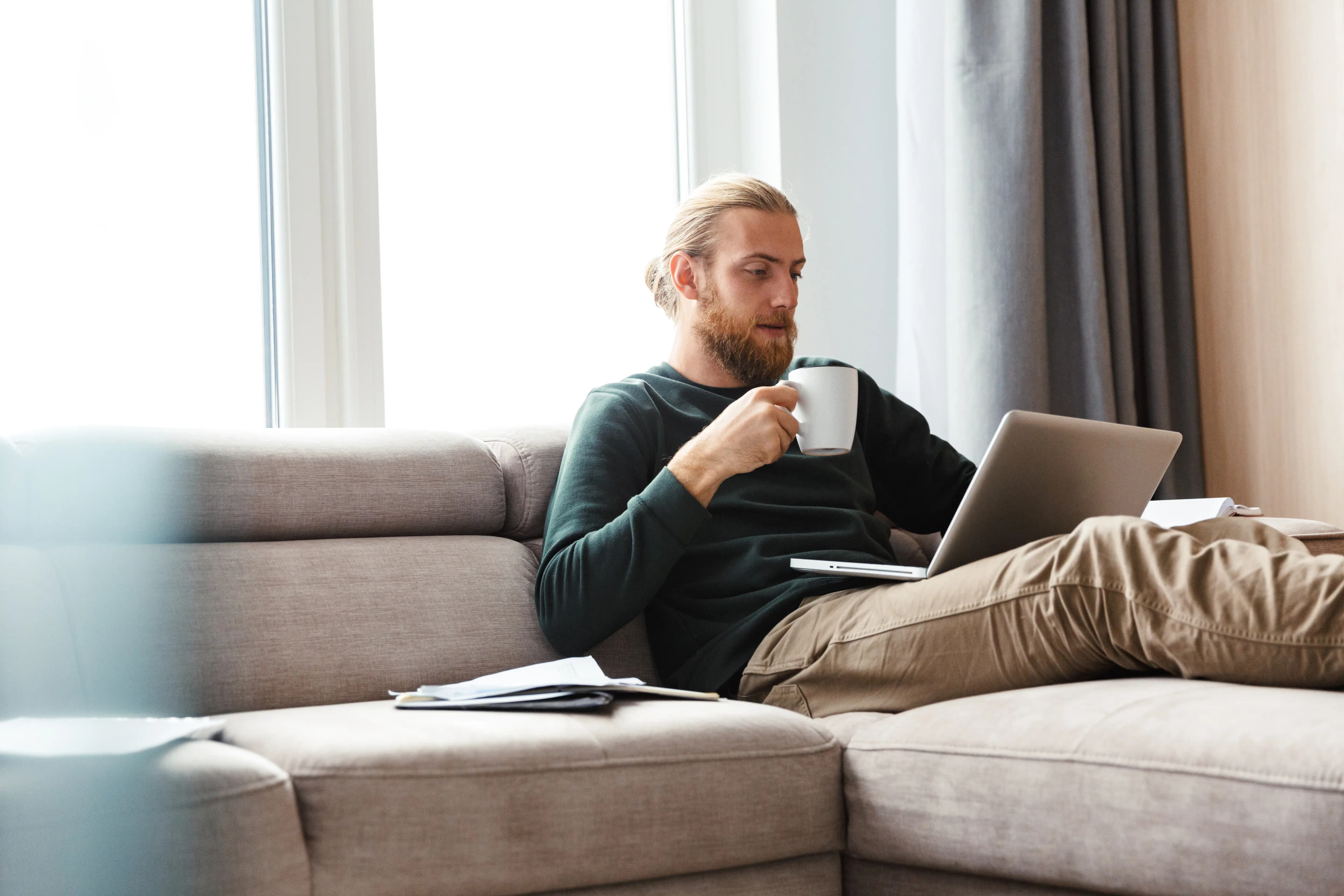 A man sits on his sofa at home, comfortable, considering his home insurance costs.