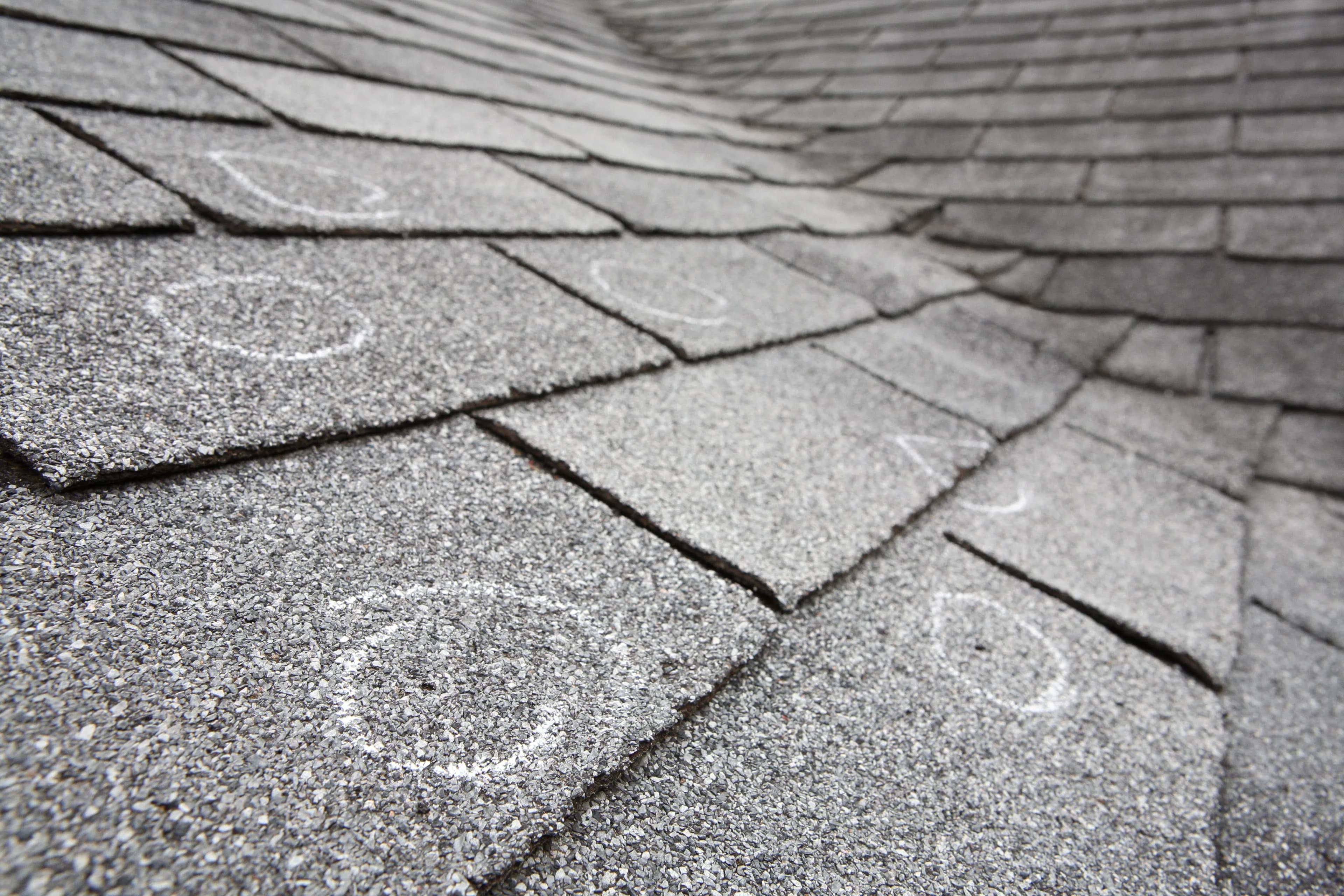 A homeowner's shingled roof displaying minor hail damage marked with chalk