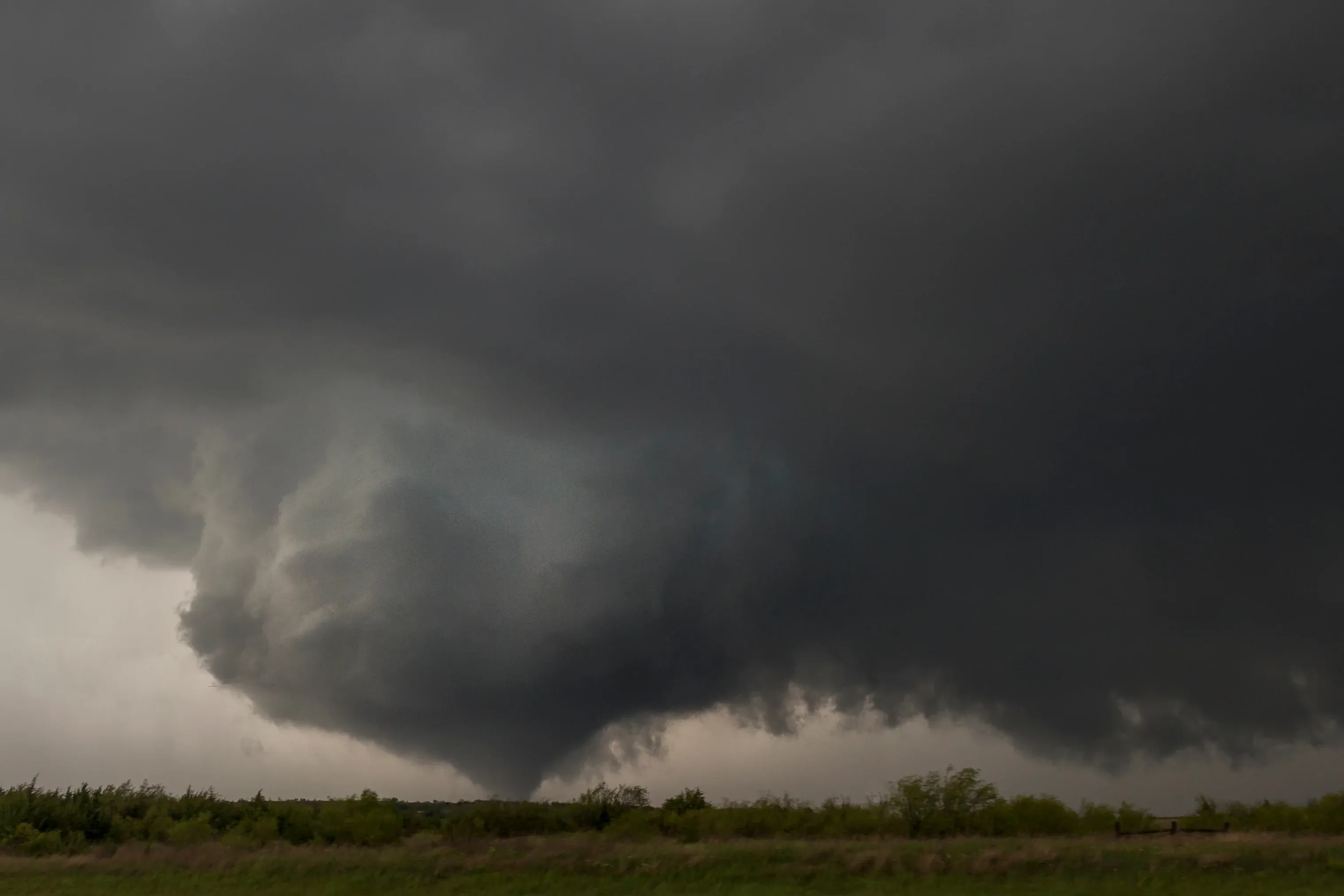 A large tornado hangs low in the sky over a field in Oklahoma