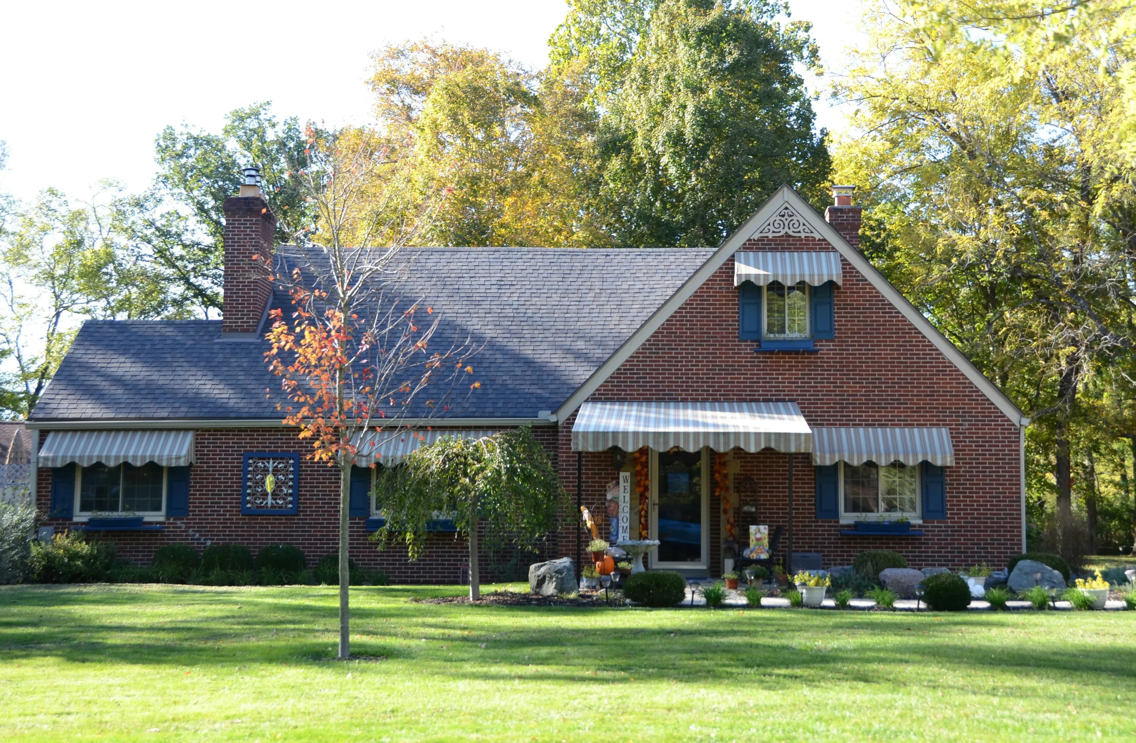 A neat, older red brick home sits among several trees in the fall.
