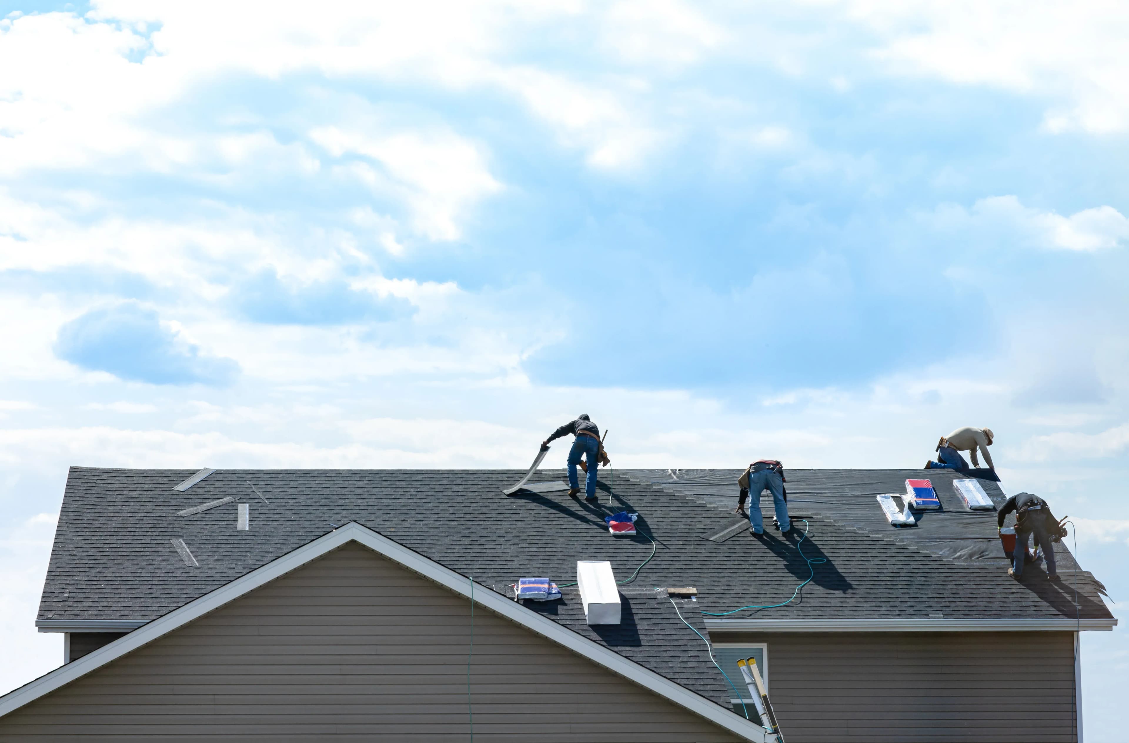 roofers work to replace missing shingles on top of a home with roof damage