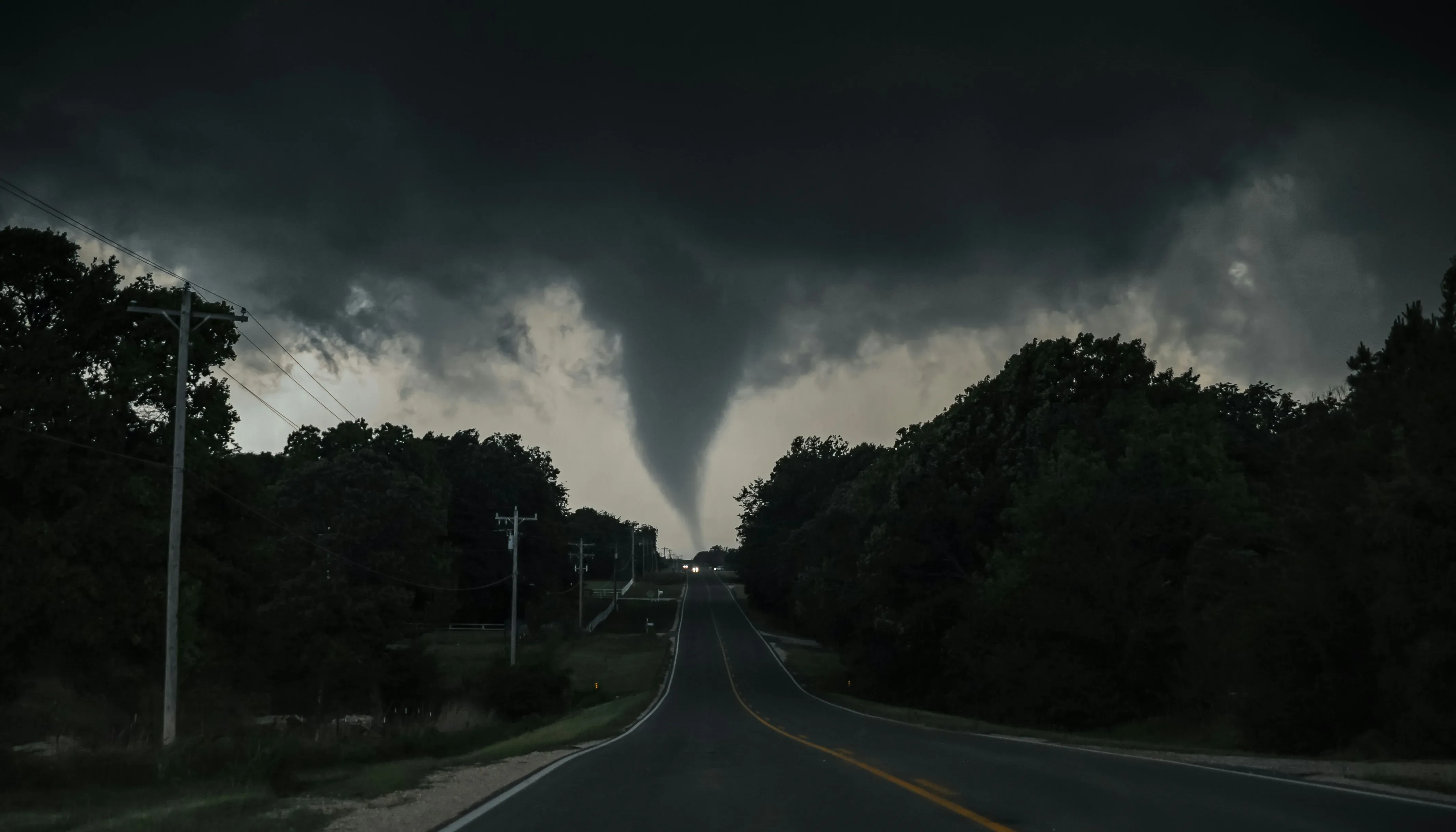 A large tornado funnel cloud touches down on a highway after a tornado warning.