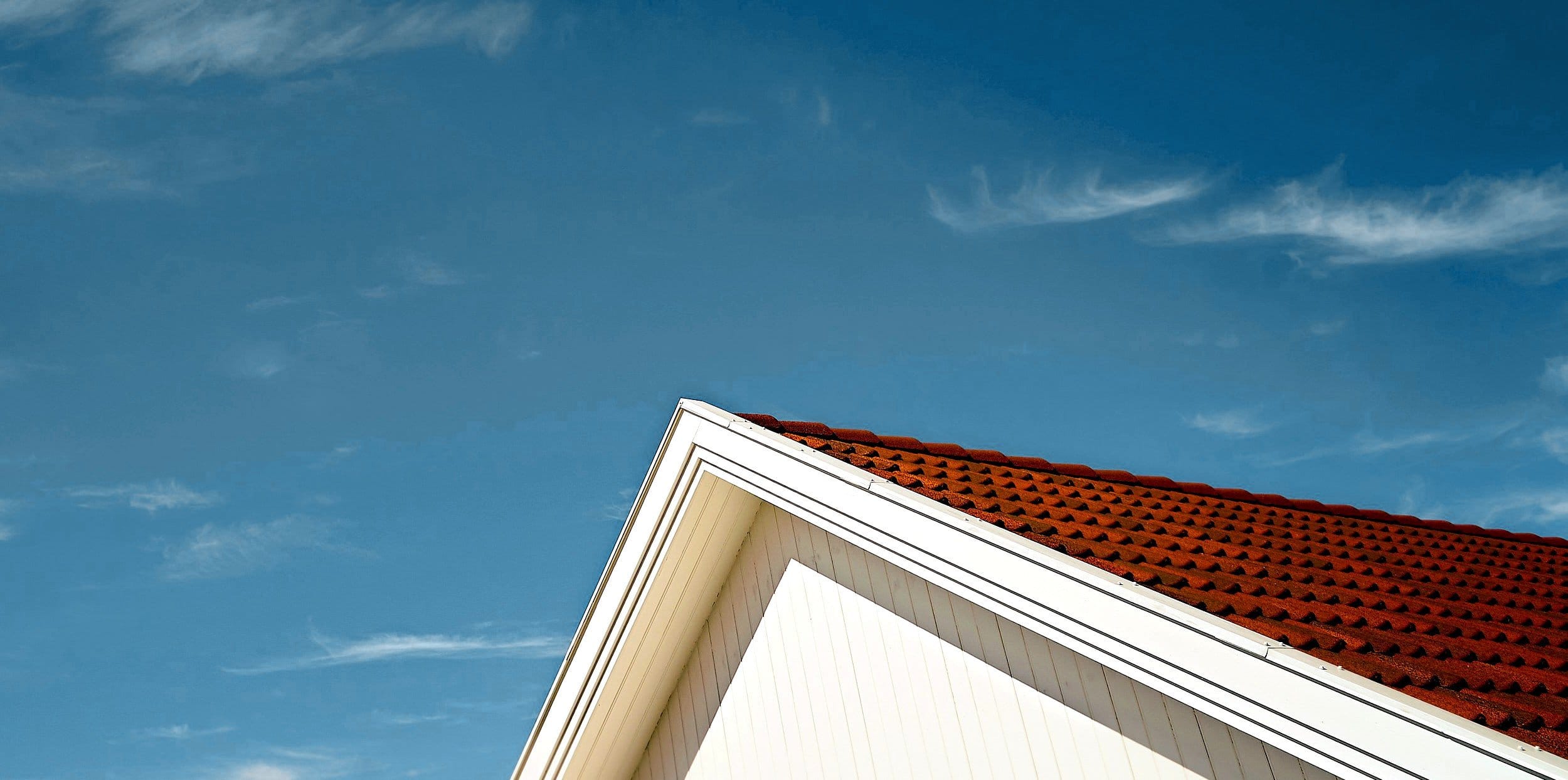 The gable of a white house with a red tile roof against a deep blue sky