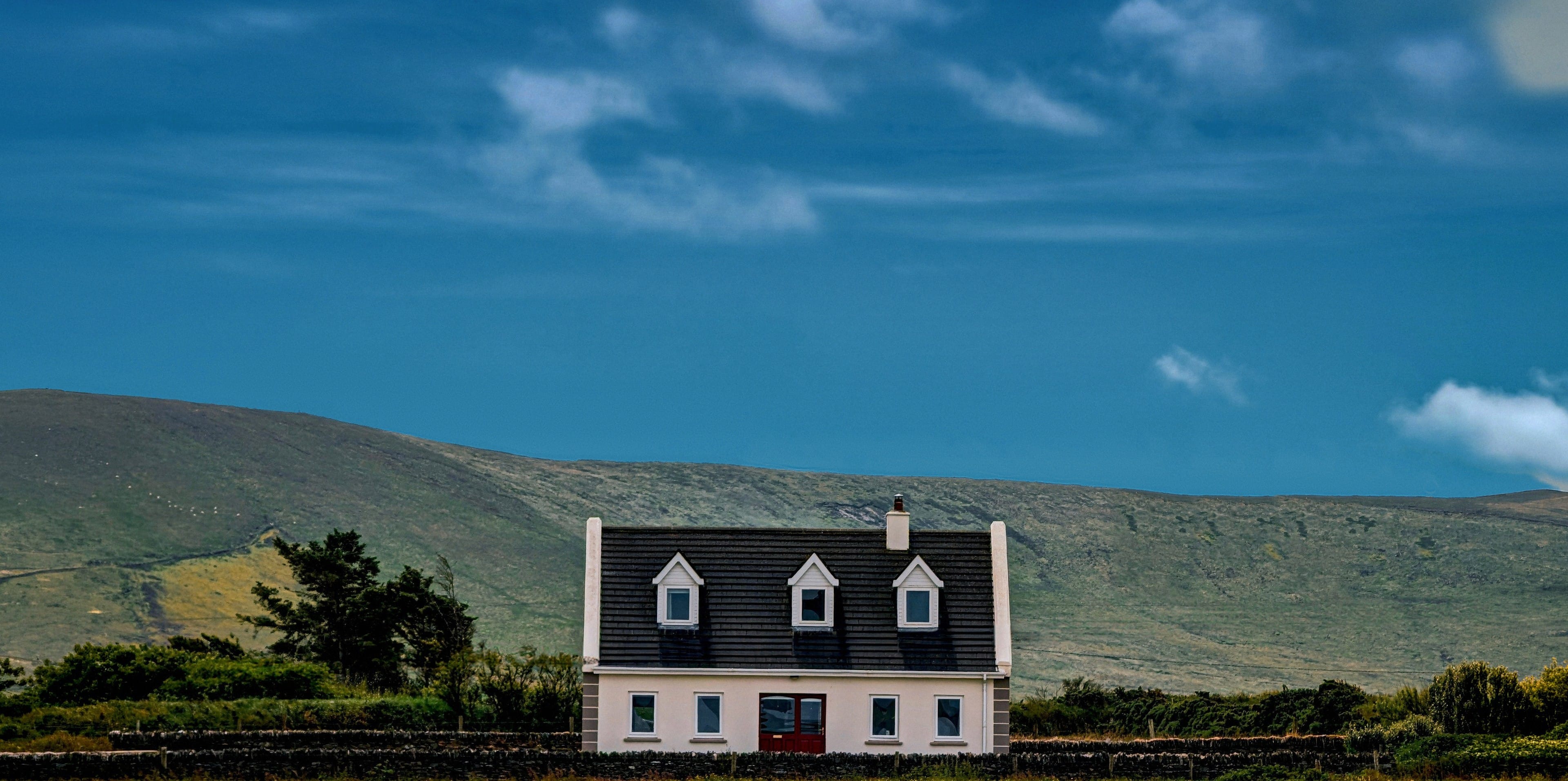 A white cottage with a slate roof in a field below a green hillside