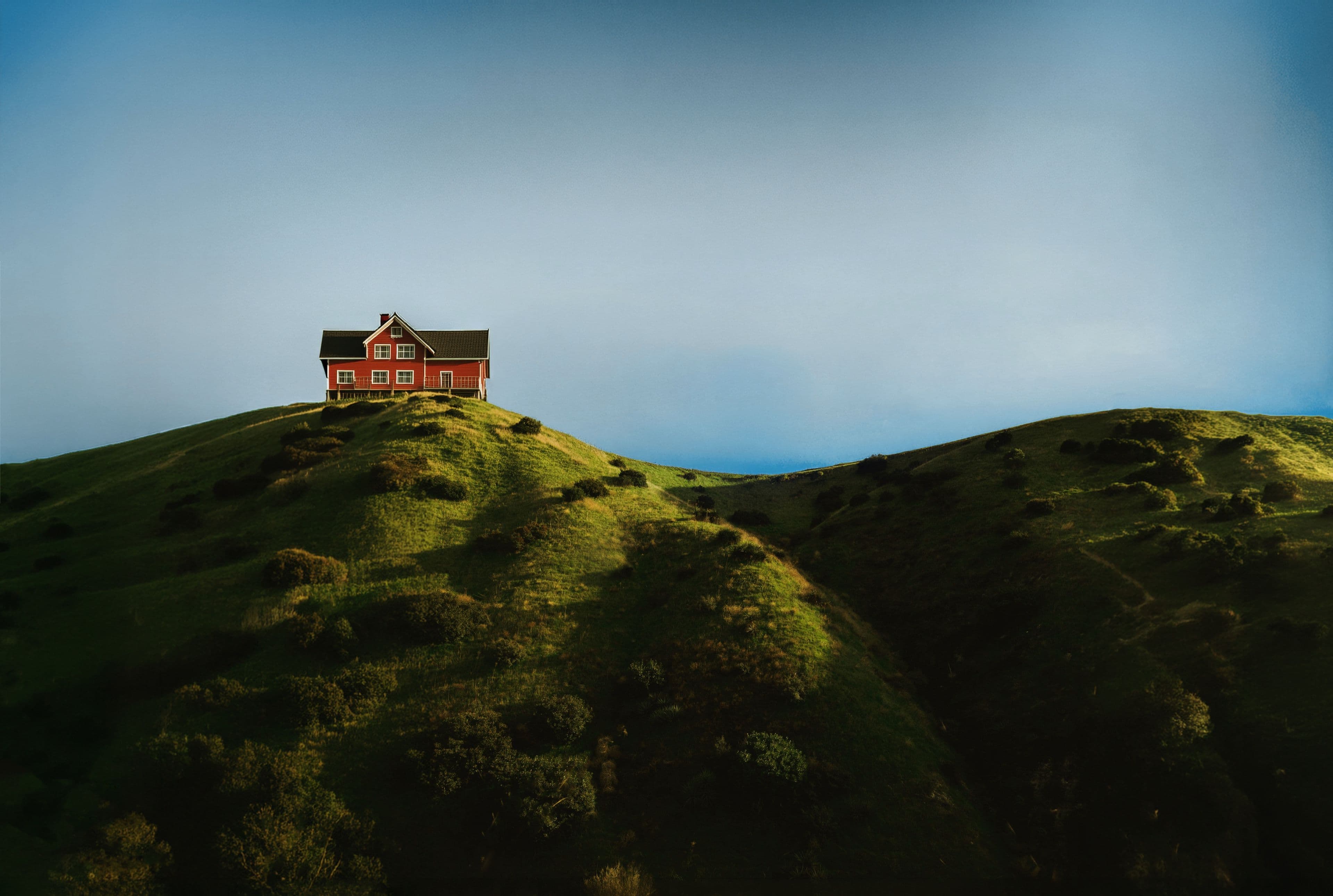 A red house standing on rolling green hills beneath a clear sky
