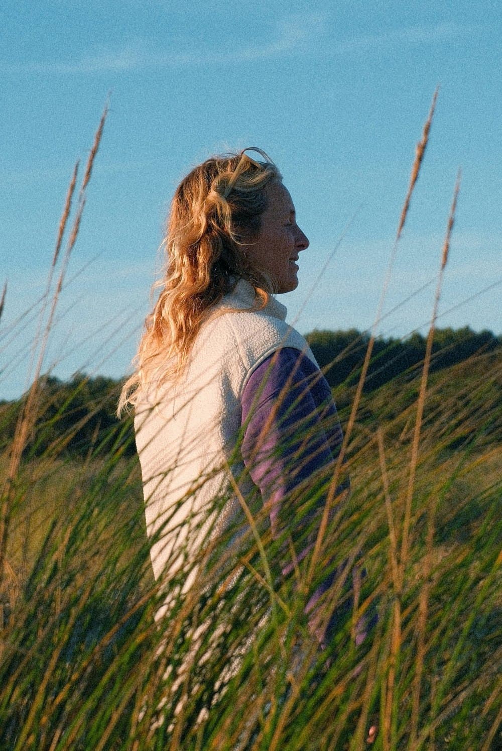 A woman standing in tall dune grass at golden hour