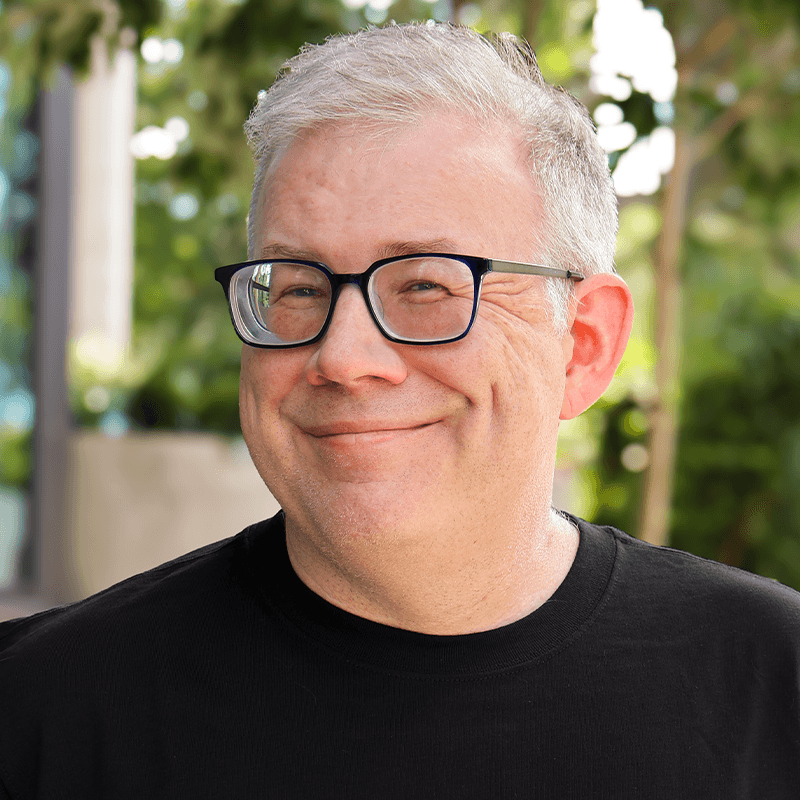 a man in a black tshirt and glasses standing outside.