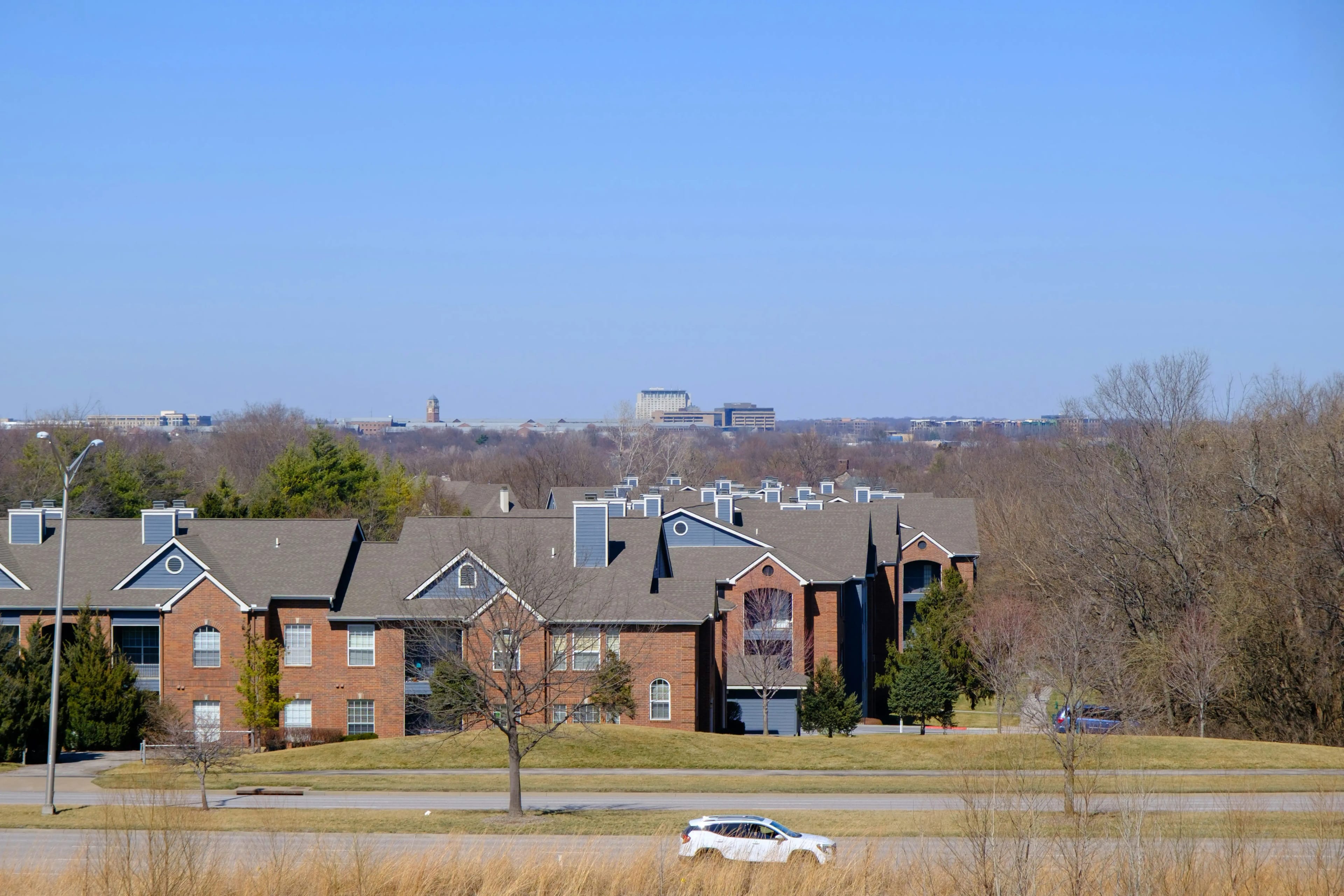 A row of townhomes in Kansas under a clear blue sky. A road runs alongside the buildings. Kansas City is visible in the distance.