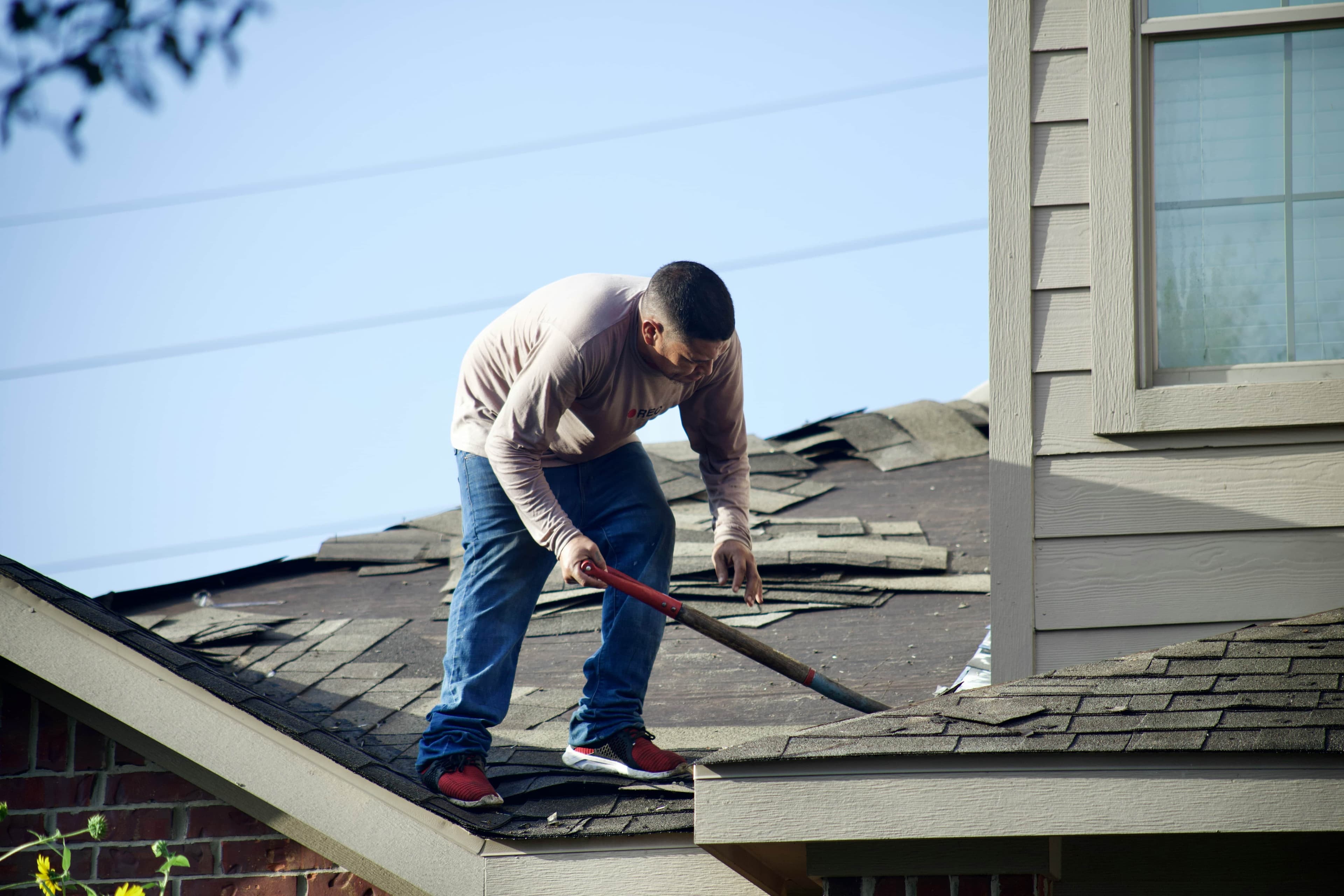 A man stands on the damaged roof of a home in Texas, repairing the missing shingles.