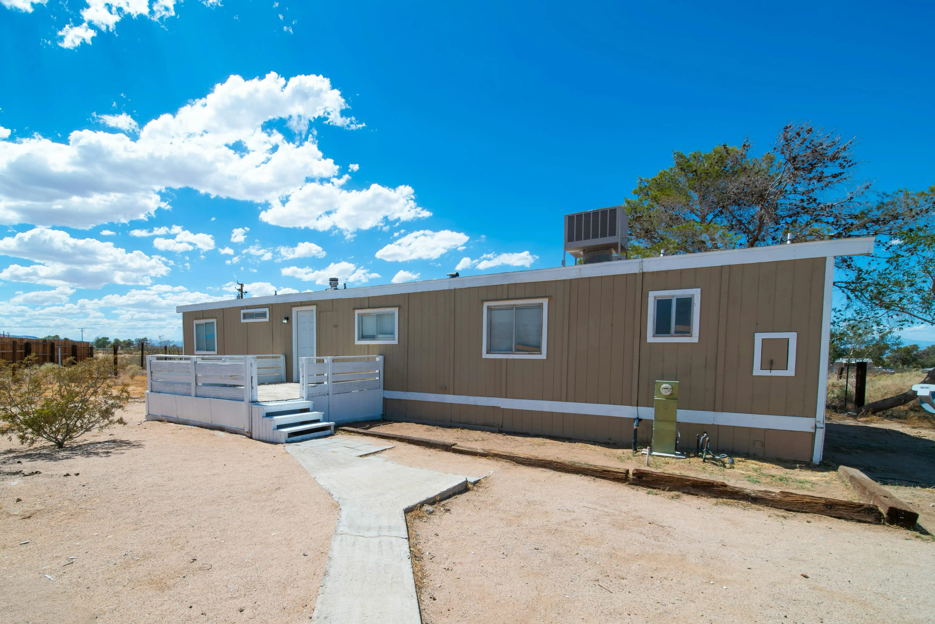 A stationary manufactured home with a built-on deck and concrete walkway.