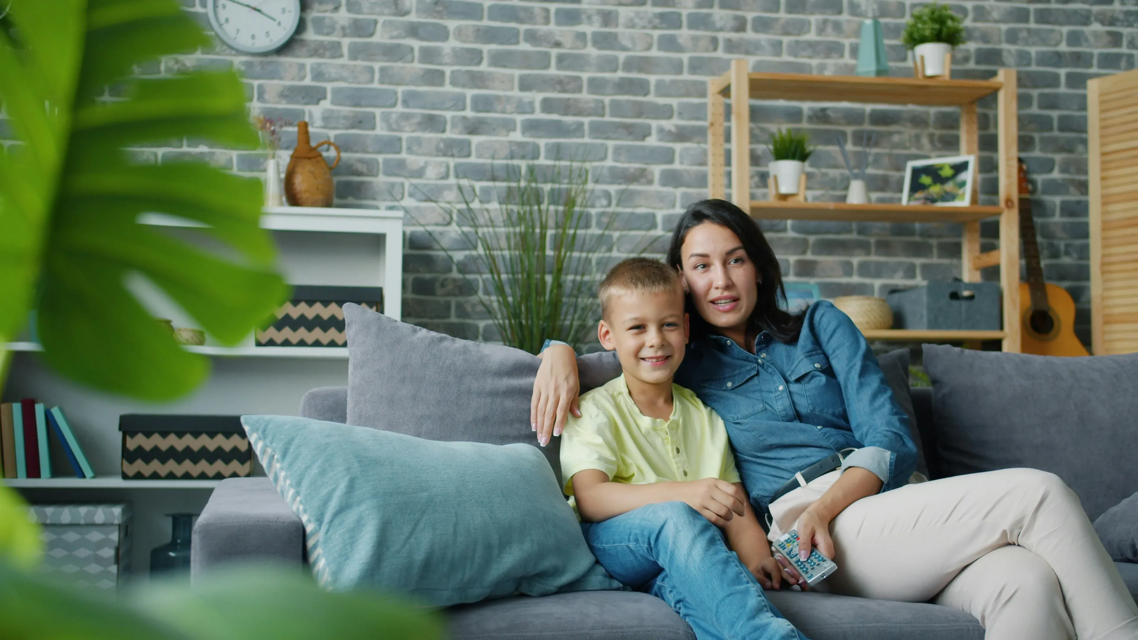 A mother and child are seated on a sofa, safe at home.
