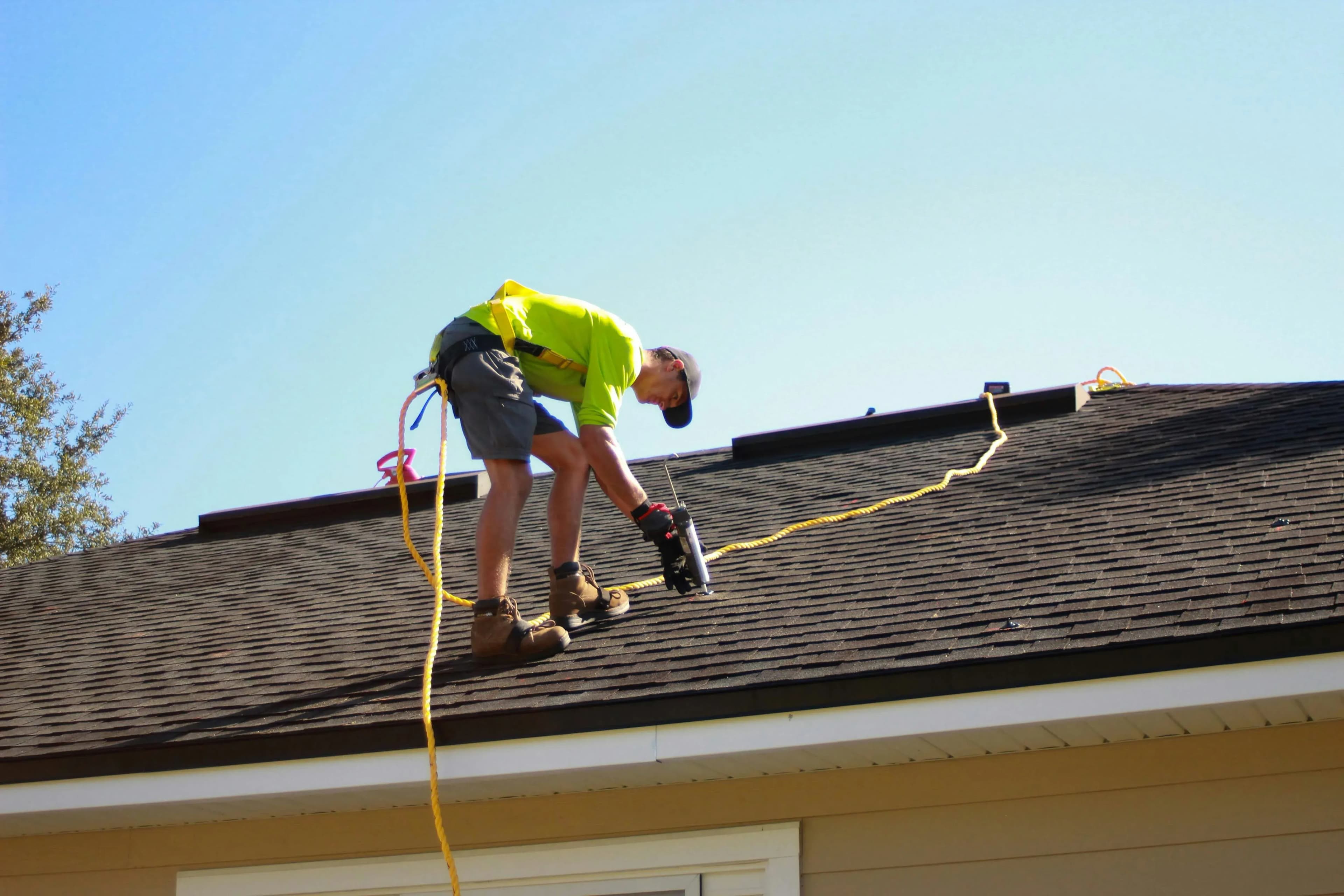 A professional roofer stands on the roof of a house, making repairs.