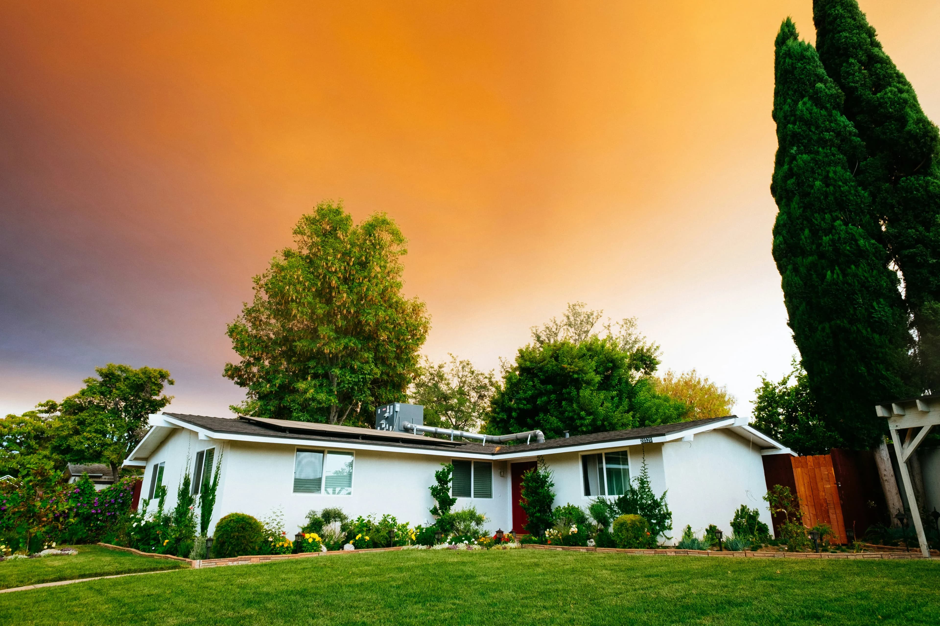 A small home sits under dusky, cloudy sky. There are two trees behind the house.