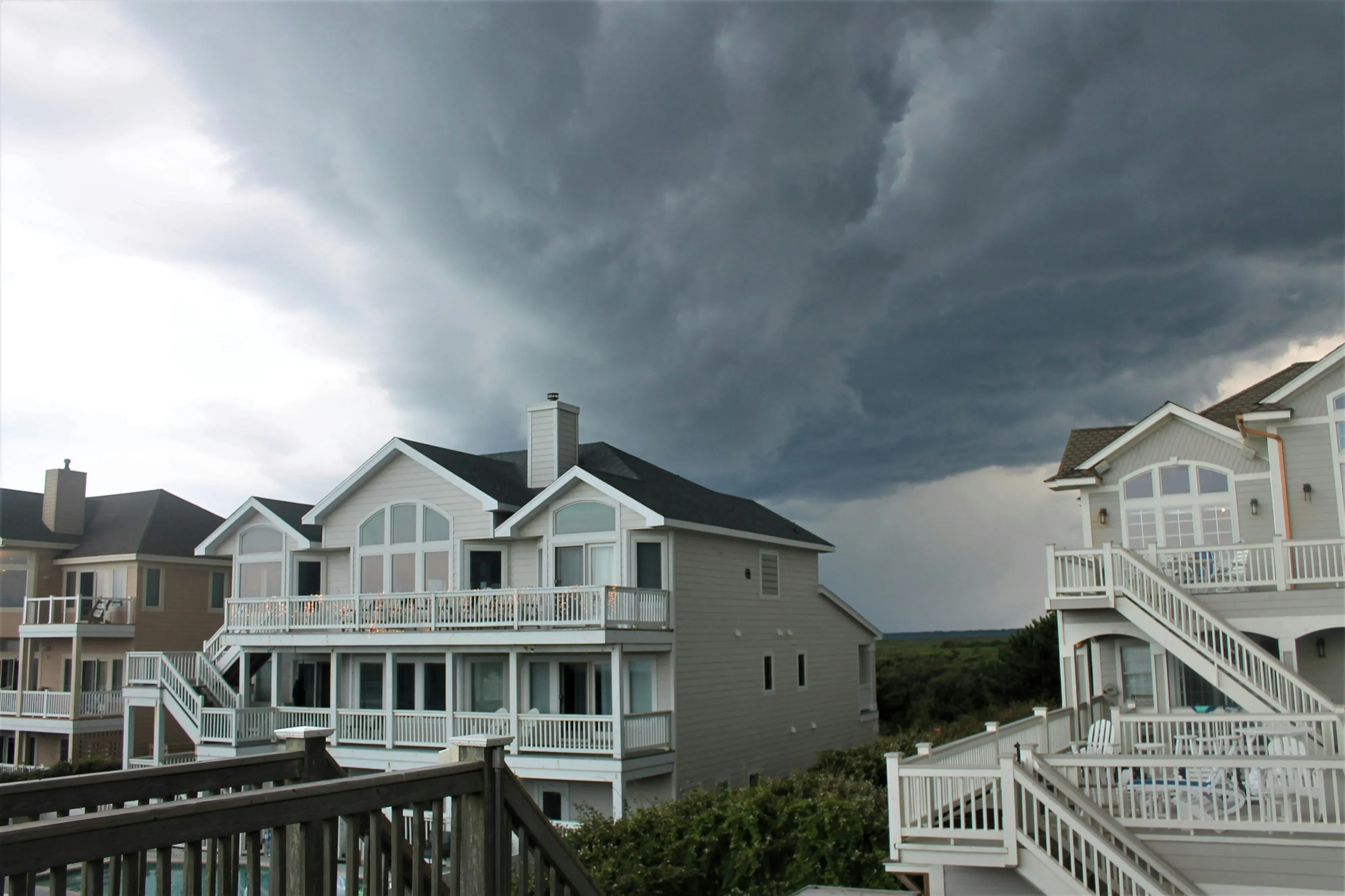 Severe thunderstorm clouds hang low over three large houses.