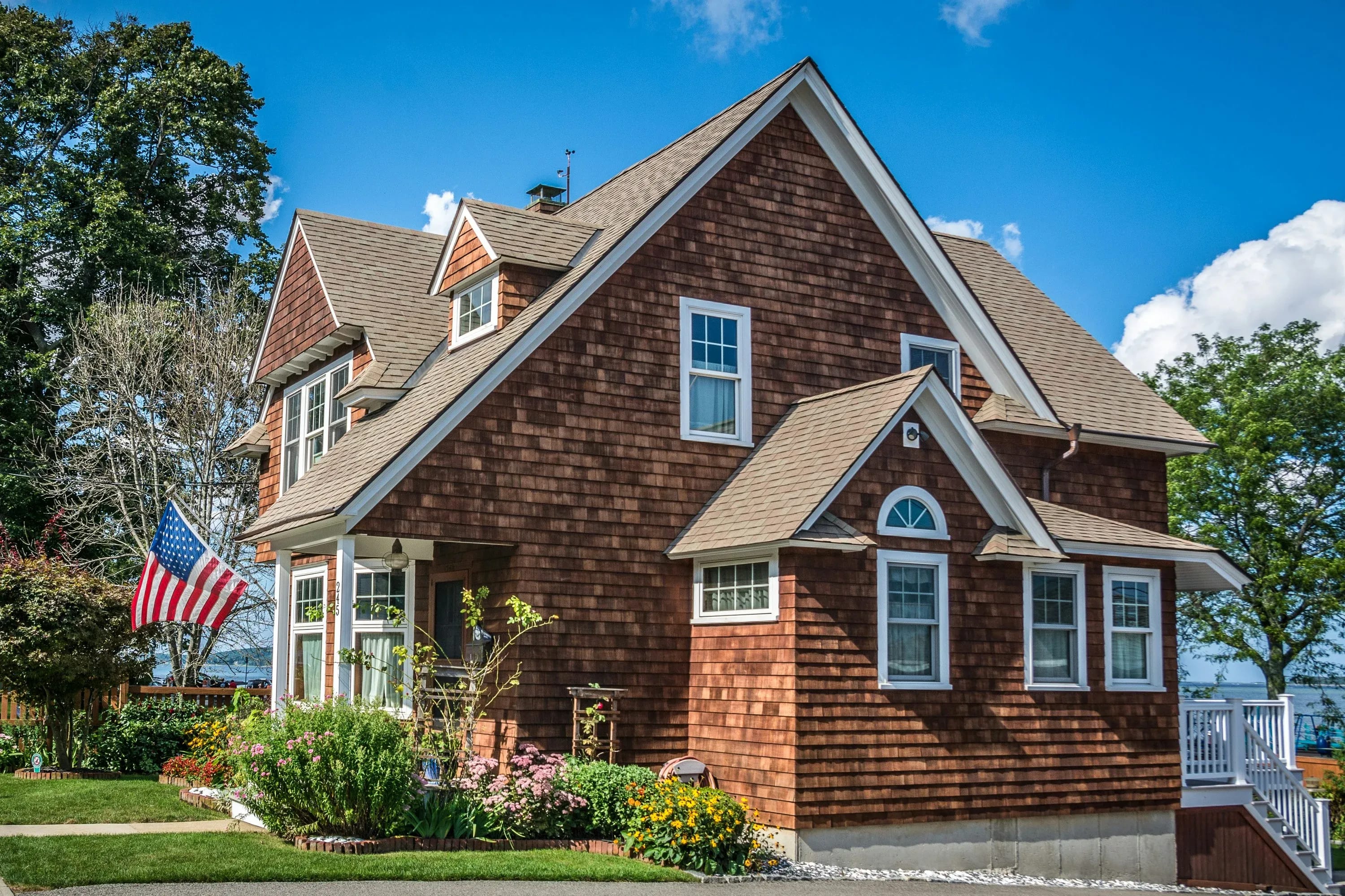 A well-maintained two-story home with an American flag sits on a wooded lawn.