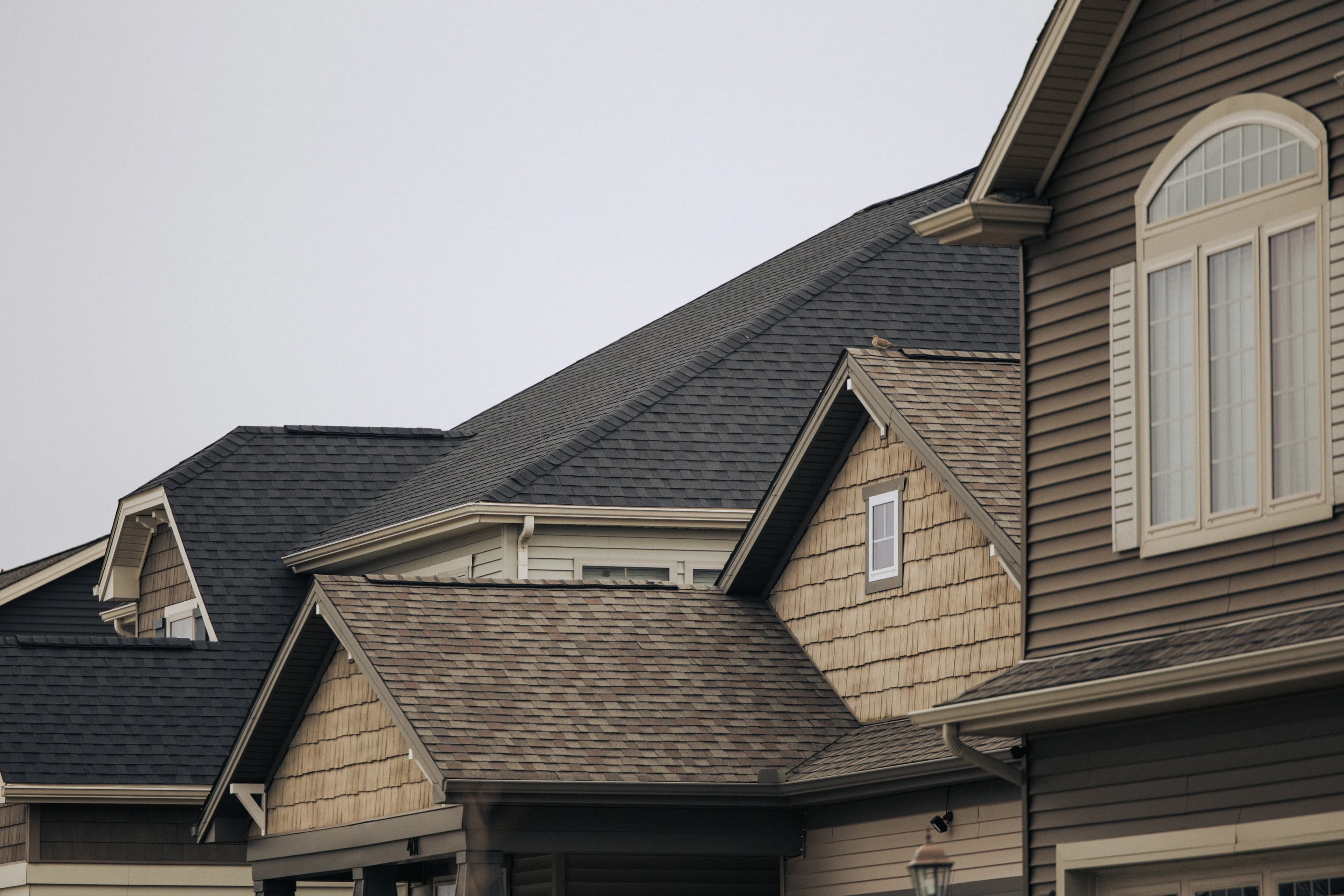 The shingled roofs of two homes, next door to each other, with a cloudy sky overhead.