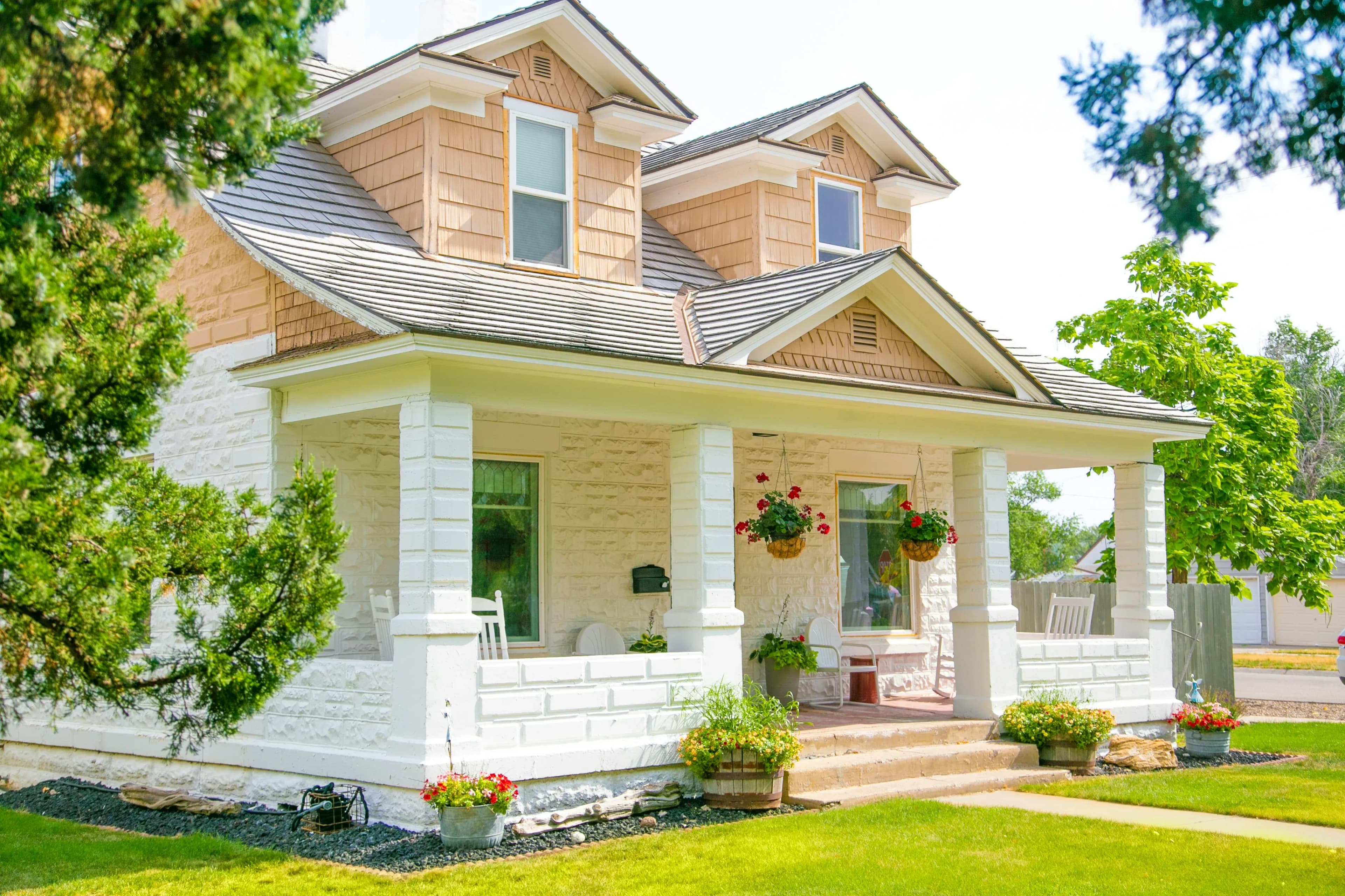 A neat two-story house with a front porch sits on a green lawn under clear skies.